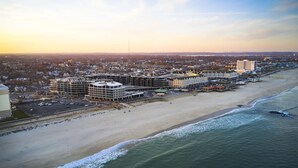 An aerial view of a coastal cityscape with a beachfront hotel, a parking lot, and a sandy beach. - Wave Resort (Long Branch)