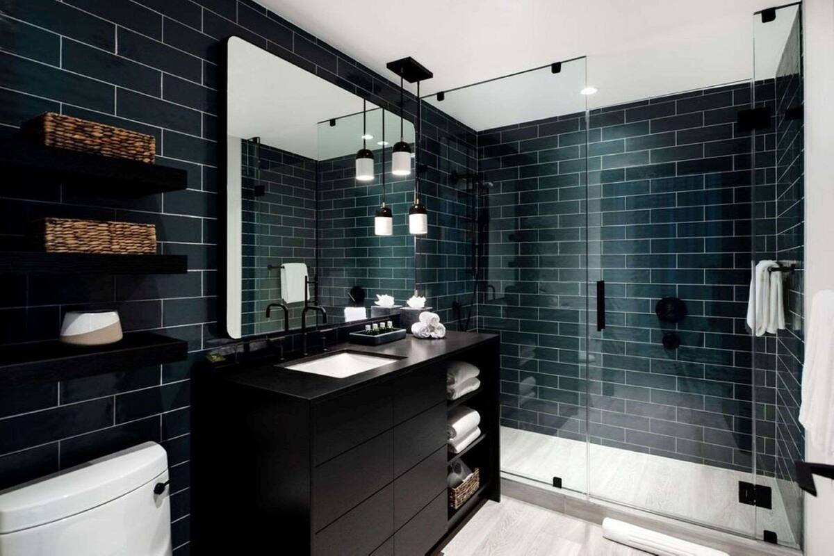 A modern bathroom with dark blue tiles, a black vanity, a large mirror, and a glass-enclosed shower.
