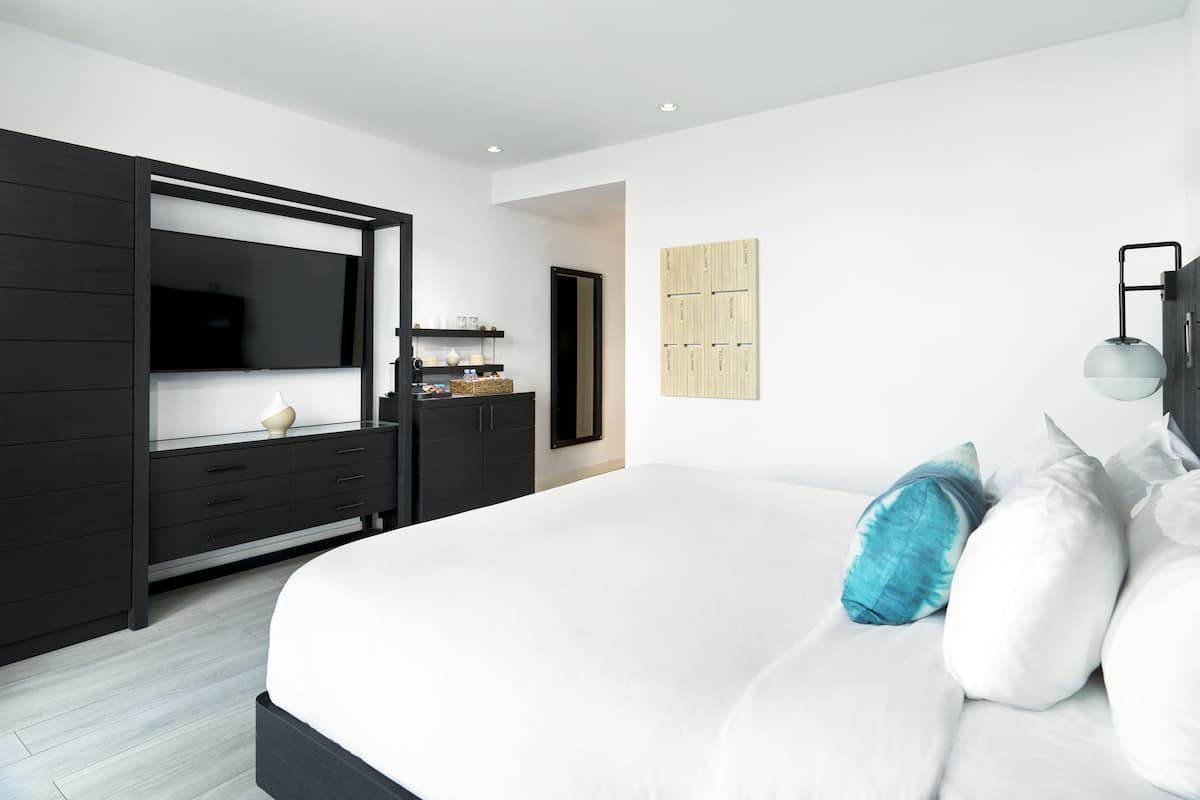 A modern bedroom with a large bed, a dark wooden wardrobe, a small bedside table, and a wall-mounted light fixture.
