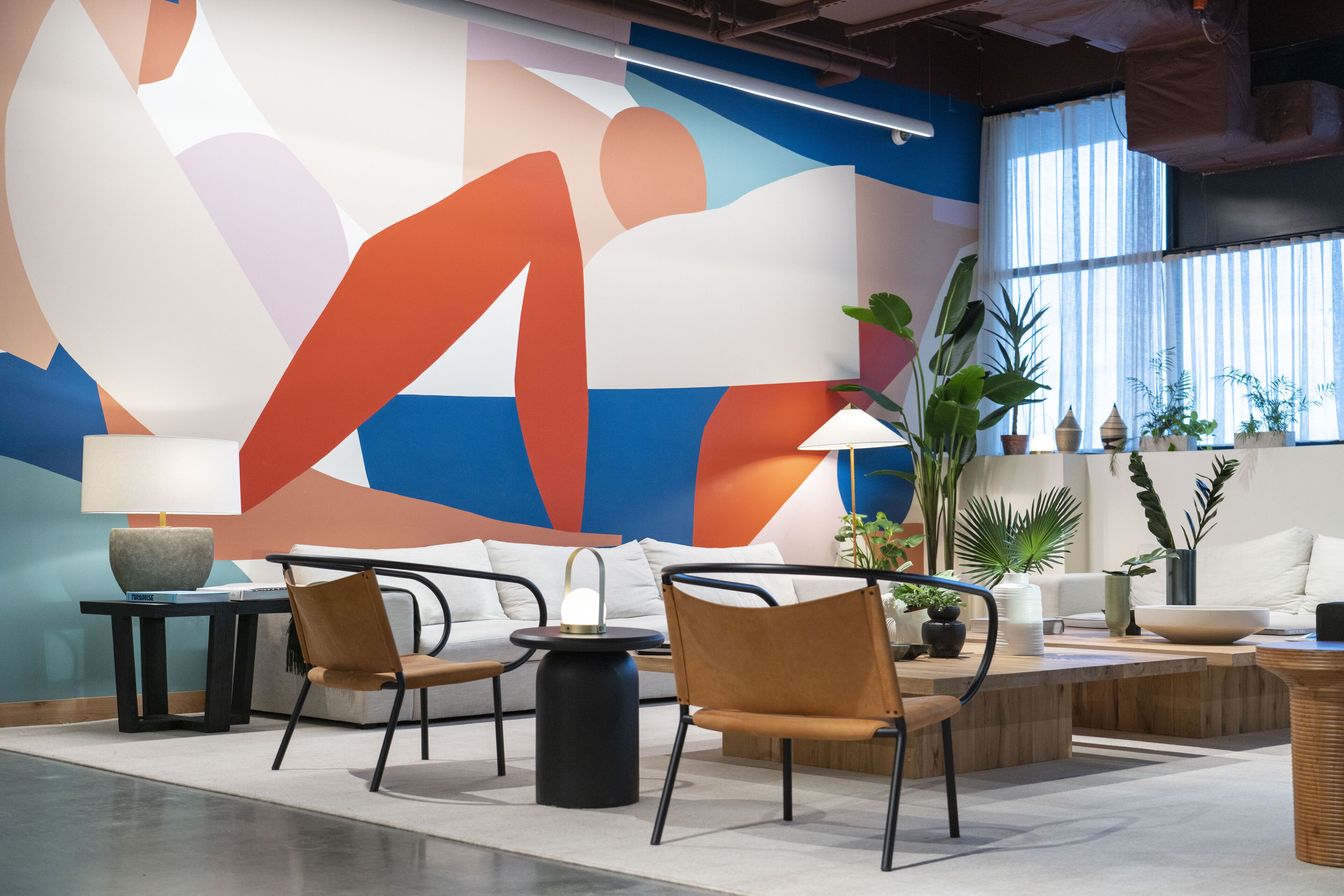 Un área de descanso moderna con un amplio mural abstracto, asientos cómodos y plantas de interior.