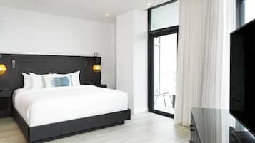 A modern hotel room with a large bed, a TV, a balcony with a chair, and a large window with curtains.