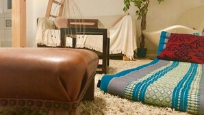 A cozy room with a brown leather ottoman, a patterned blanket, and a wooden chair with a white cushion.