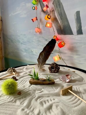 A serene indoor setting with a sand garden centerpiece featuring a feather, plants, and a wooden bowl.