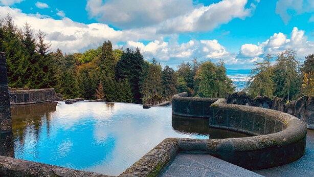 A tranquil outdoor pool surrounded by stone walls and dense forest.