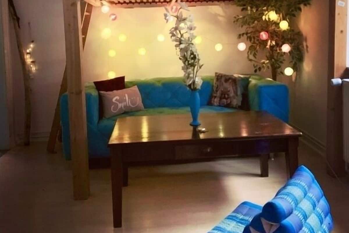 Een gezellige woonkamer met een blauwe bank, een houten salontafel en een muurschildering van een strandlandschap op het plafond.