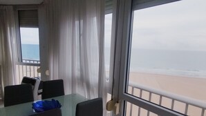 Een kamer met een glazen tafel en stoelen, uitzicht op het strand, en een balkon met een hekwerk.
