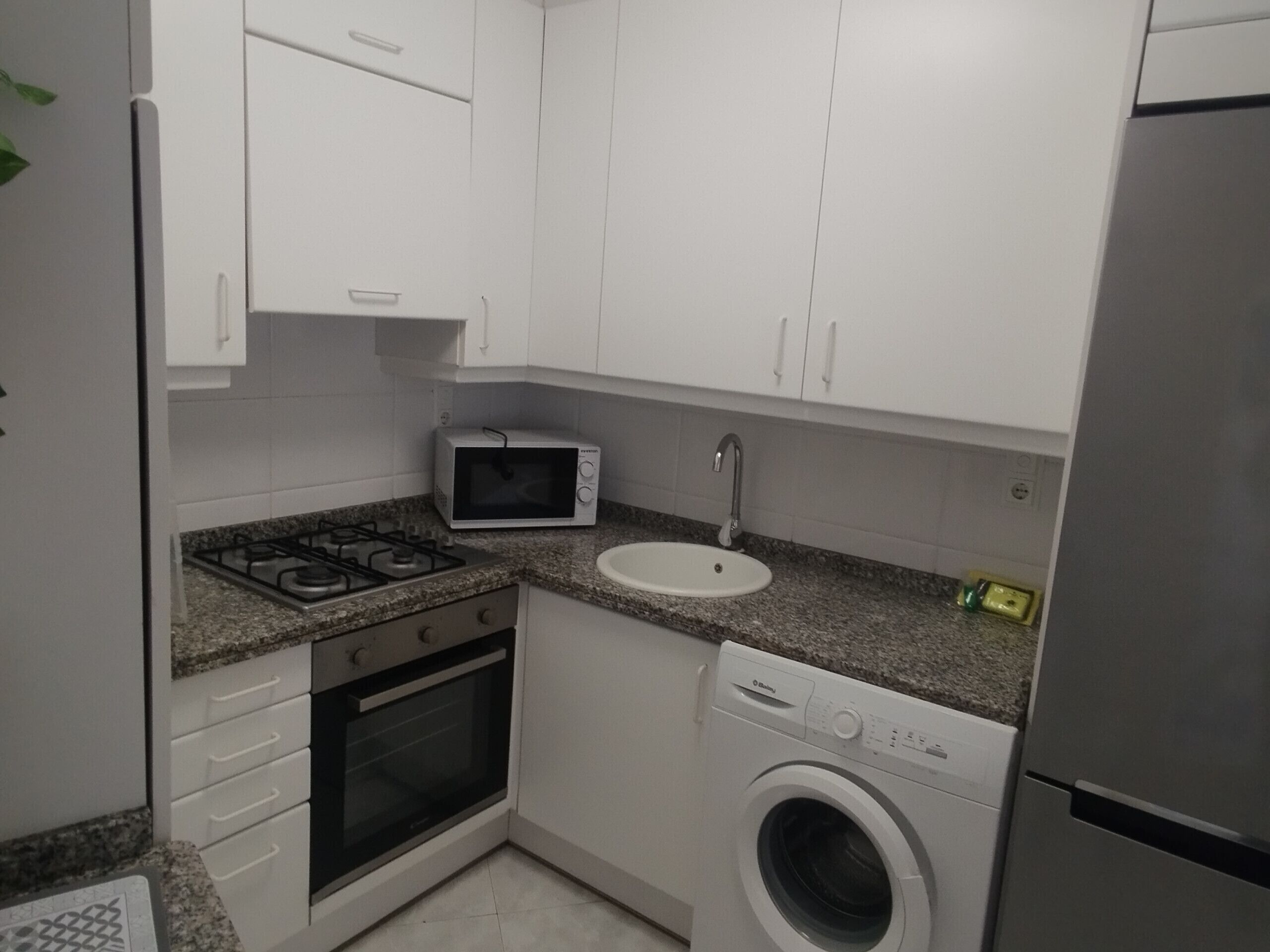 A compact kitchen with white cabinets, a microwave, a sink, a stove, an oven, and a washing machine.