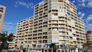 Een hotel met meerdere verdiepingen, balkons, een parkeerplaats en diverse winkels.