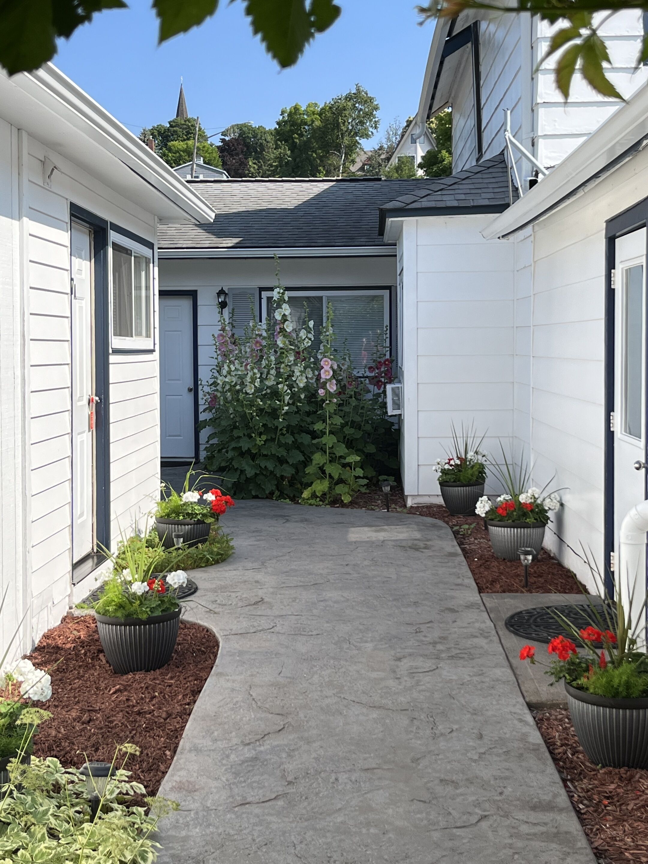 A narrow concrete pathway flanked by white buildings with black-framed windows and doors.