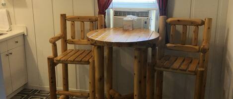 A small kitchen with a round wooden table and two chairs, a window with curtains, and a patterned floor.