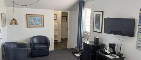 A hotel room with a large bed, a desk with a computer, a chair, a TV, and a small kitchenette.
