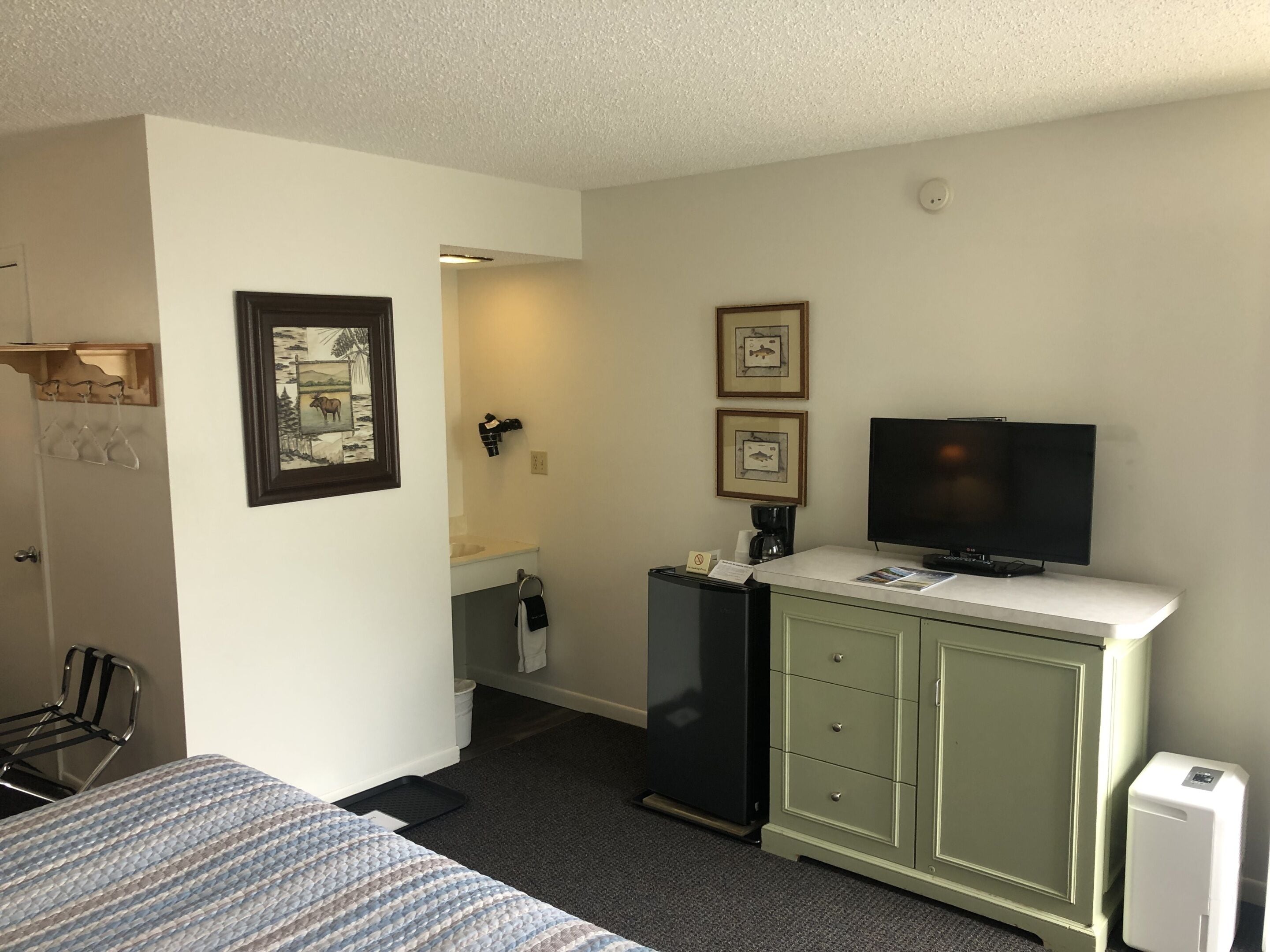 Ein Hotelzimmer mit einem Bett, einem Schreibtisch mit Computer, einem Fernseher, einem Kühlschrank und einem Badezimmer.