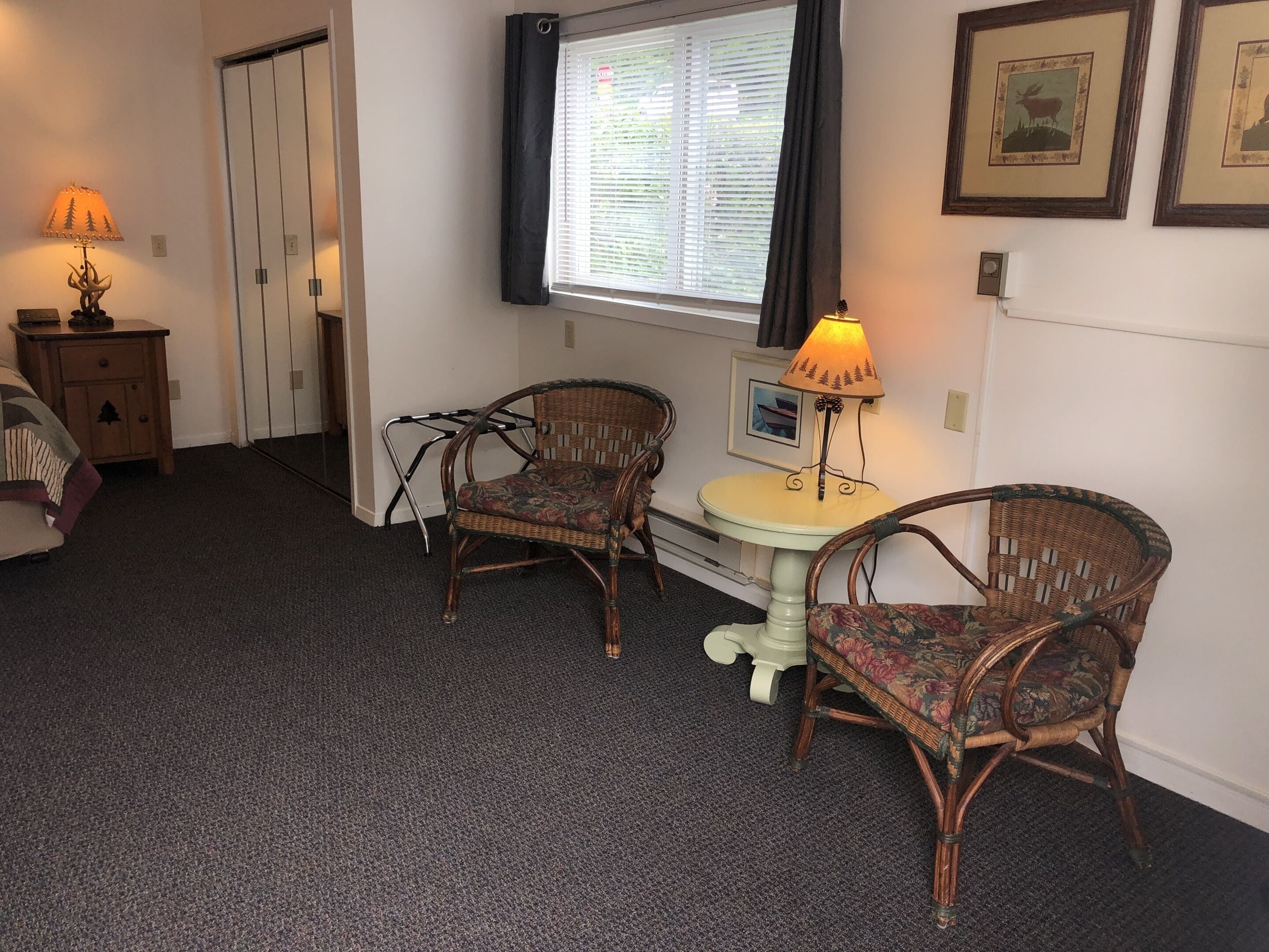 A room with two wicker chairs, a small round table, a lamp, and a window with blinds.