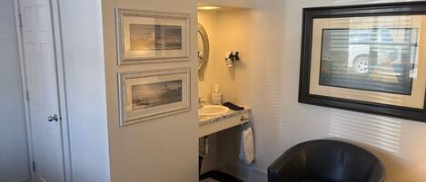 A bathroom with a white door, a sink with a mirror, and a framed picture on the wall.