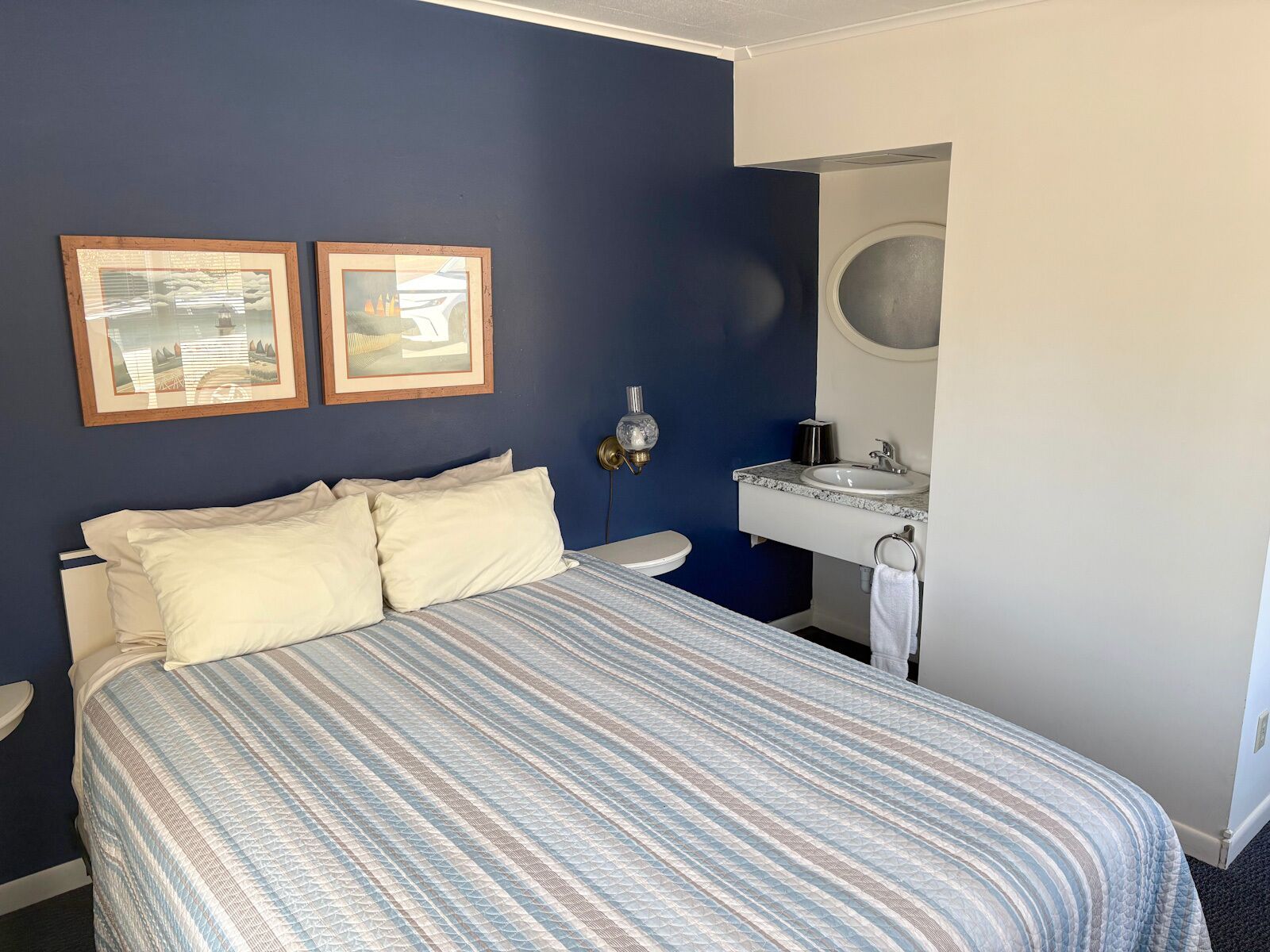 Una camera da letto con un letto, due quadri appesi, un comodino, un lavandino e uno specchio.