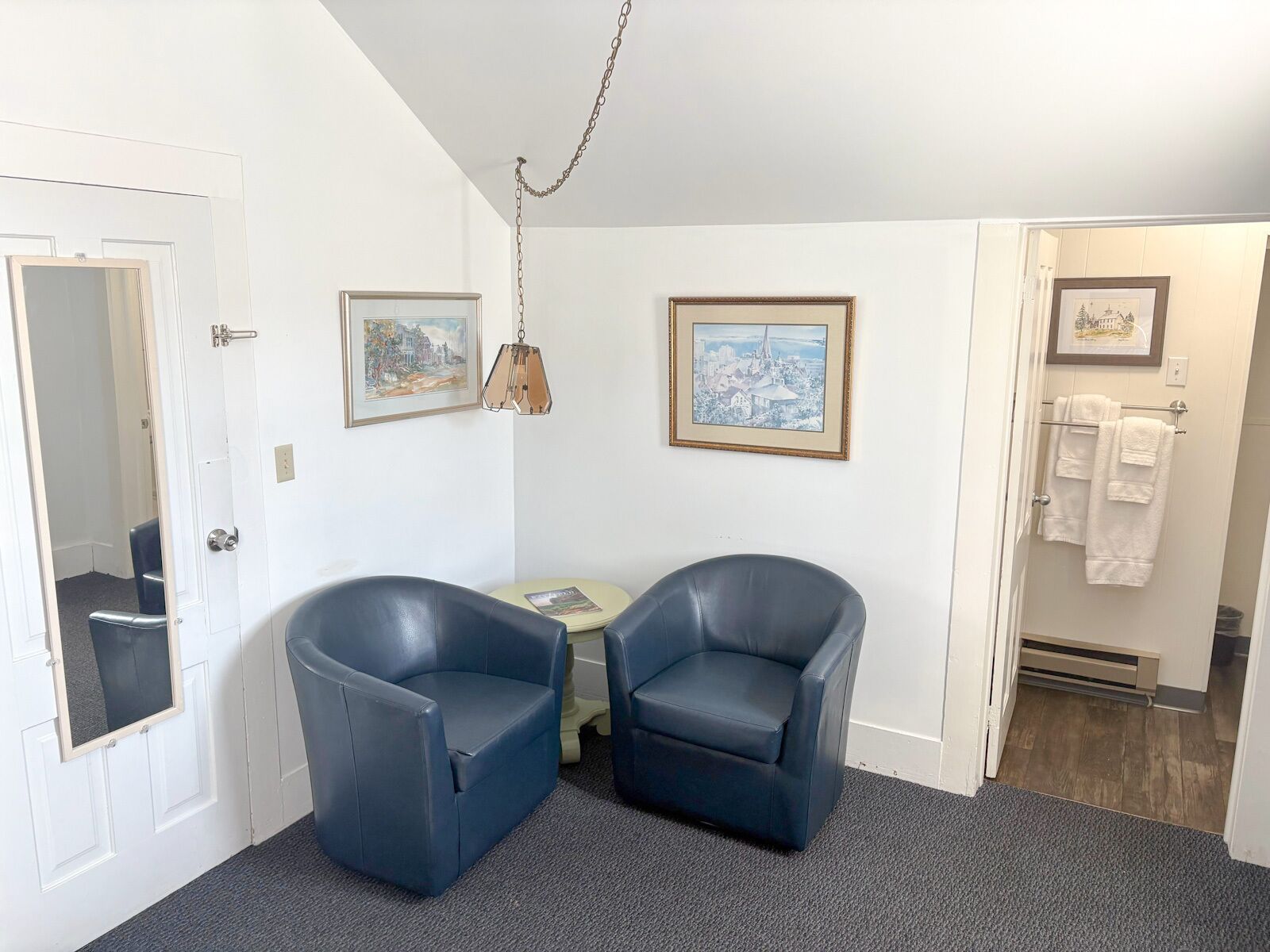 A room with two dark blue chairs, a small table, and two framed pictures on the wall.