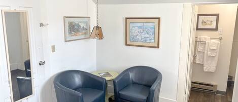 A room with two dark blue chairs, a small table, and two framed pictures on the wall.