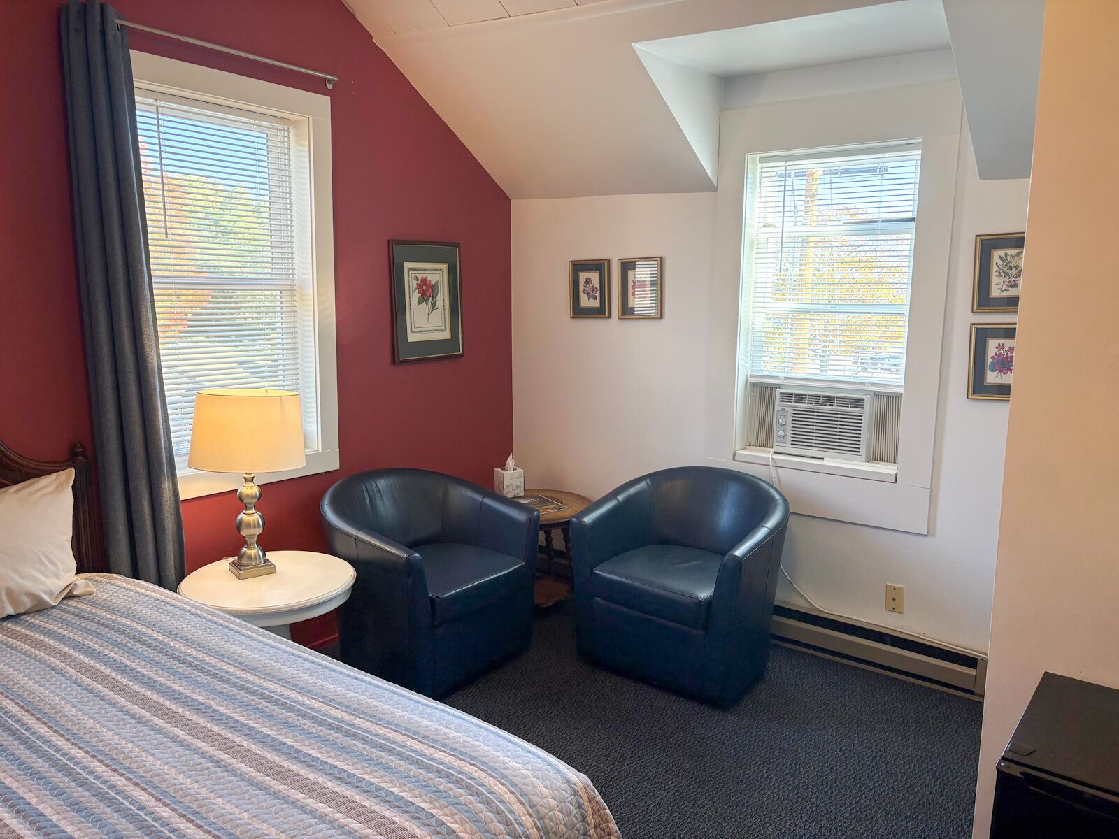 Een hotelkamer met een bed, twee fauteuils, een tafeltje en een raam met luxaflex.