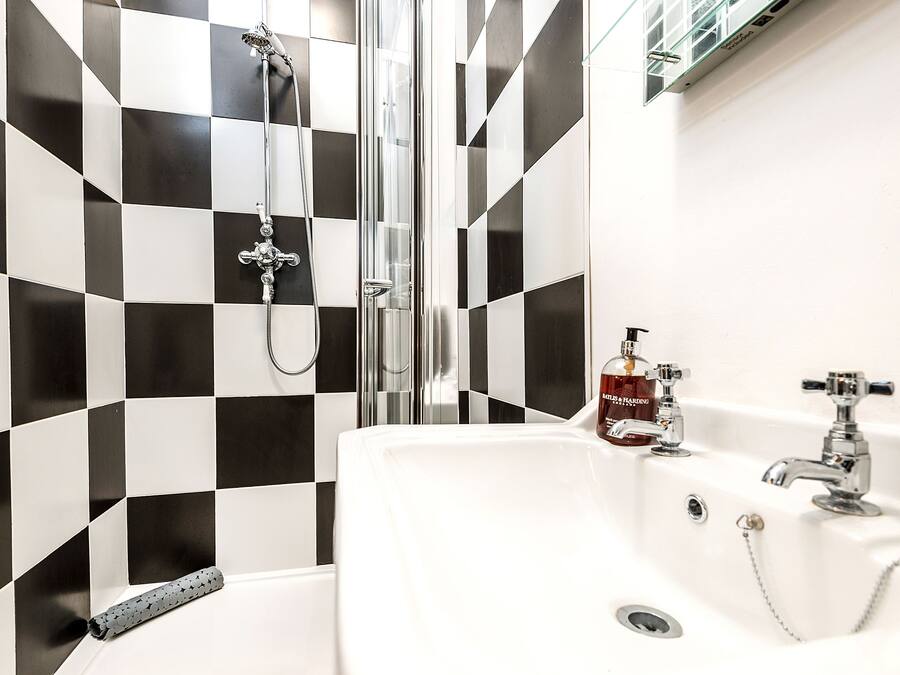 A bathroom with a checkered black and white tile wall, a glass-enclosed shower, a white sink with a chrome faucet, and a bottle of hand soap on the counter.