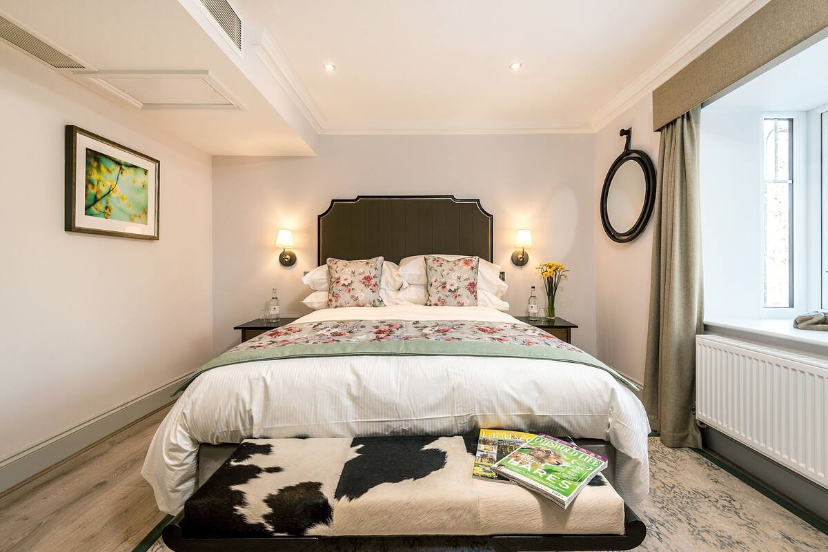 A bedroom with a bed, a nightstand, a wall-mounted mirror, a window with curtains, and a framed picture on the wall.