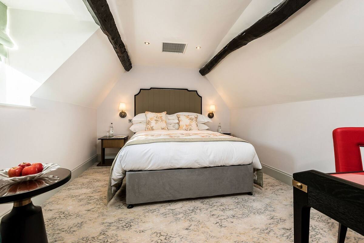 A bedroom with a bed, a nightstand, a red chair, and a table with apples.