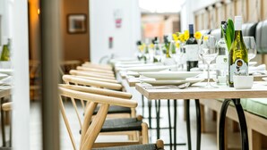 Un restaurante con sillas y mesas de madera, cada conjunto con platos, cubiertos y copas de vino.