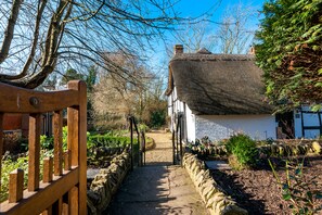 A narrow stone pathway leading to a traditional thatched-roof house with a white exterior, surrounded by greenery and a wooden gate. - Burnside Hotel (Stratford-upon-Avon)