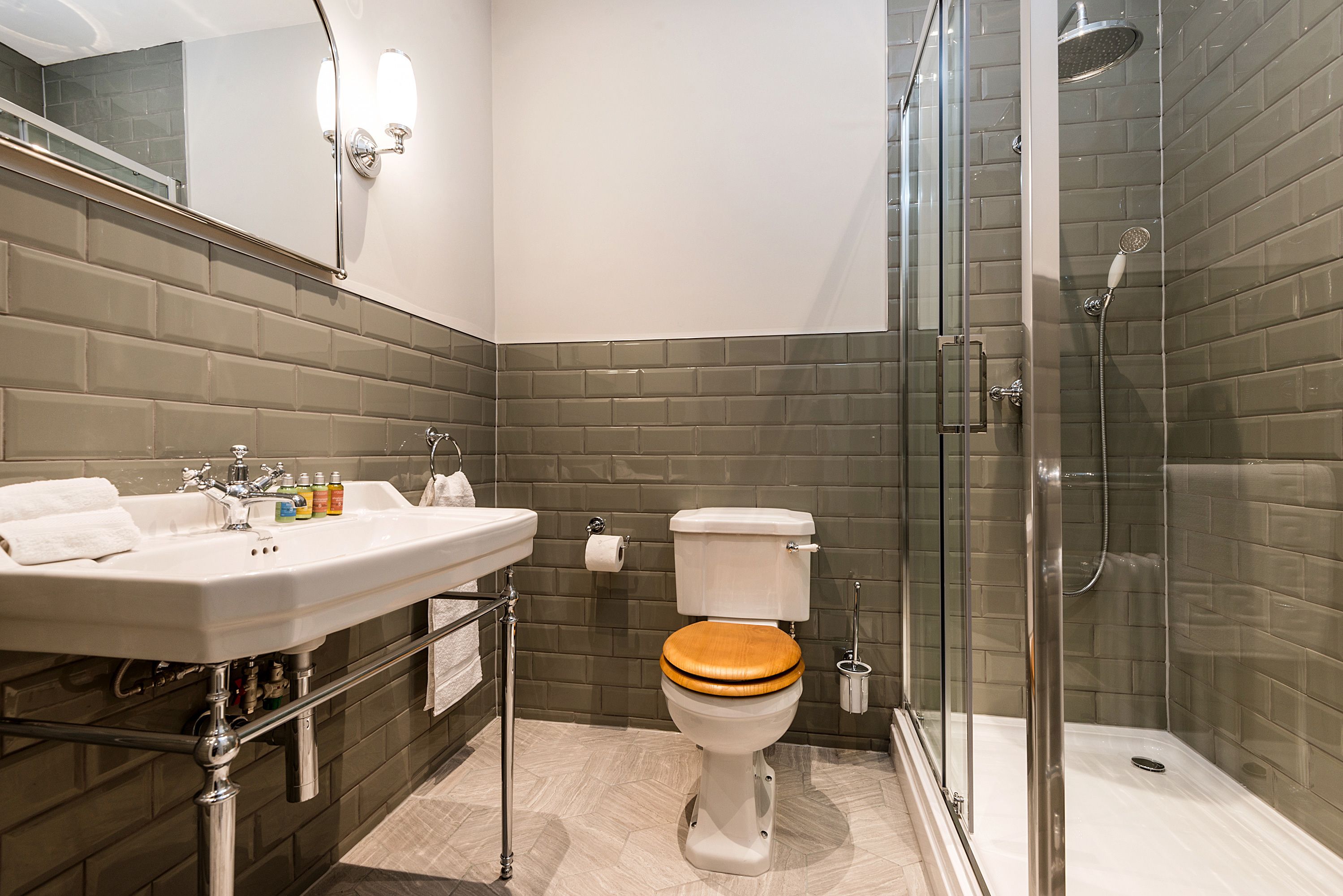 Un baño moderno con ducha de vidrio, un lavabo blanco con espejo y un asiento de inodoro de madera.