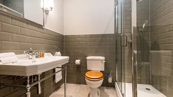 Un baño moderno con ducha de vidrio, un lavabo blanco con espejo y un asiento de inodoro de madera.