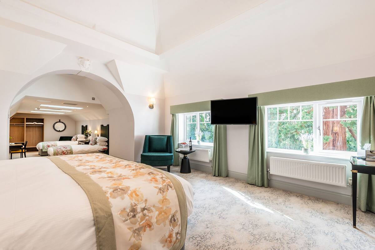 A spacious bedroom with a large bed, a desk, a chair, and a television.