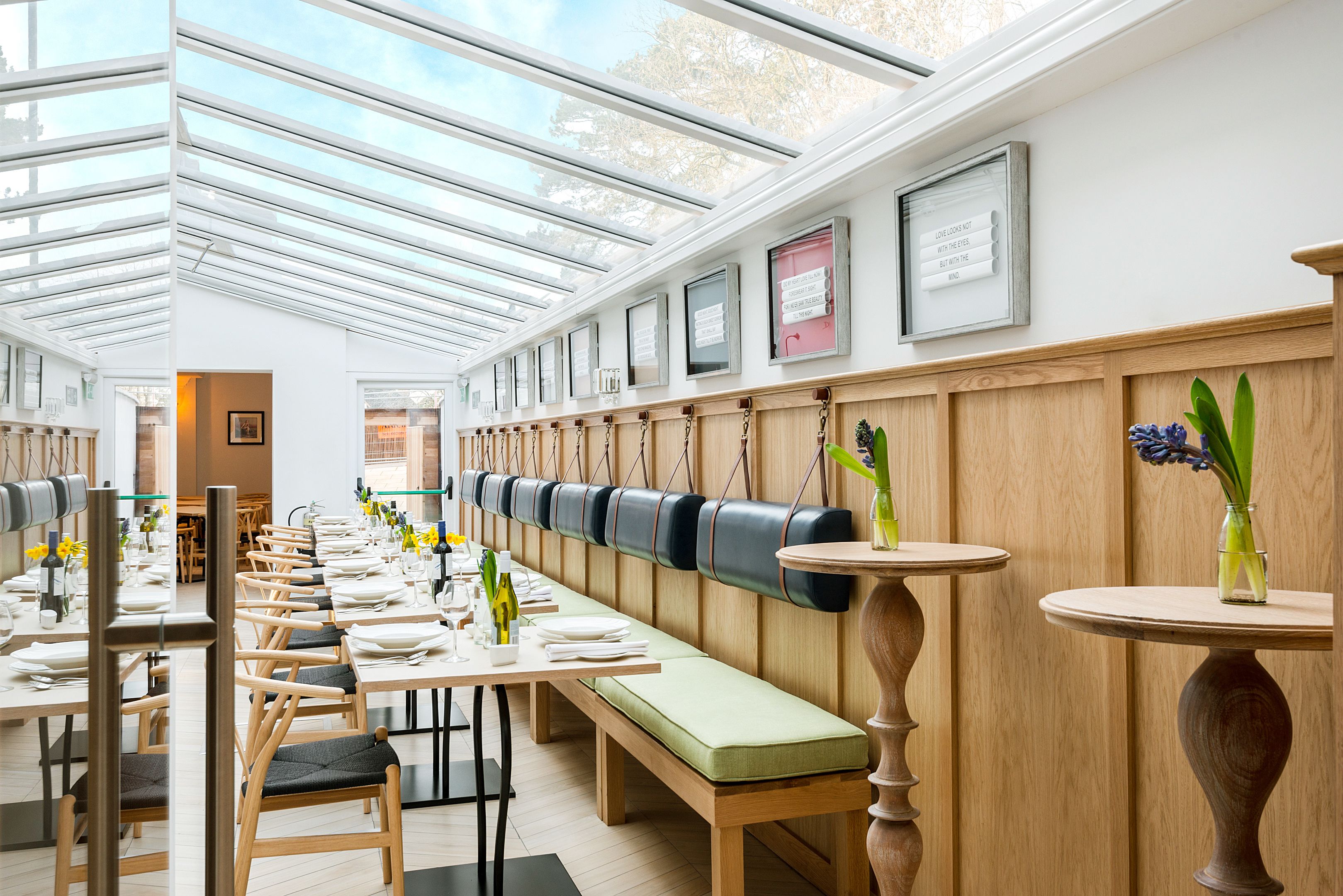 A restaurant with long wooden tables, cushioned benches, and a high ceiling with skylights.