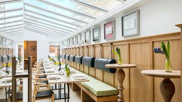 A restaurant with long wooden tables, cushioned benches, and a high ceiling with skylights.