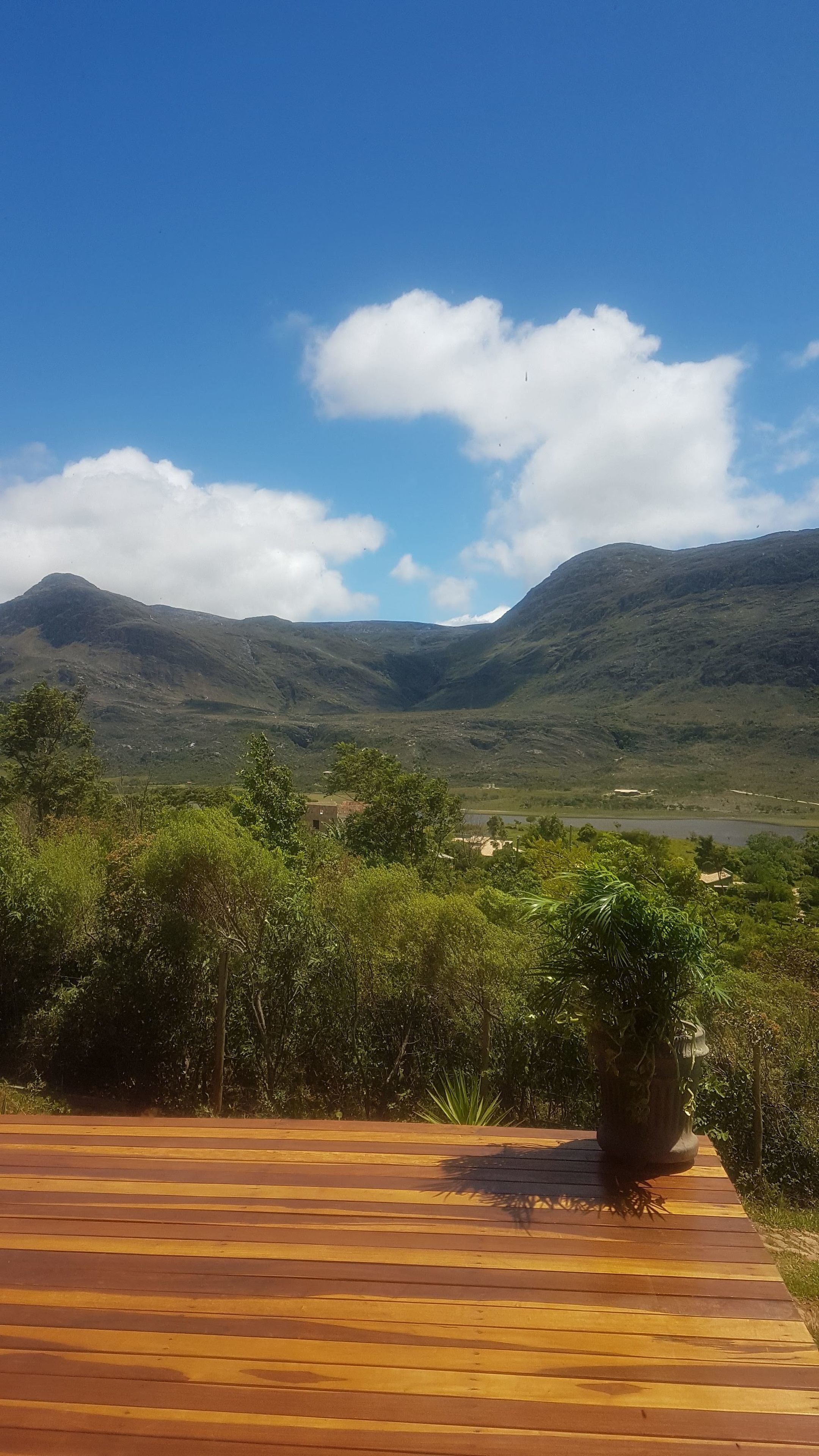 Una terraza de madera con vista a un valle y montañas bajo un cielo despejado.