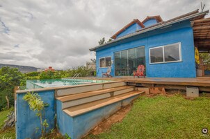 Una casa azul con piscina, escalones que llevan a una terraza y un ventanal grande.