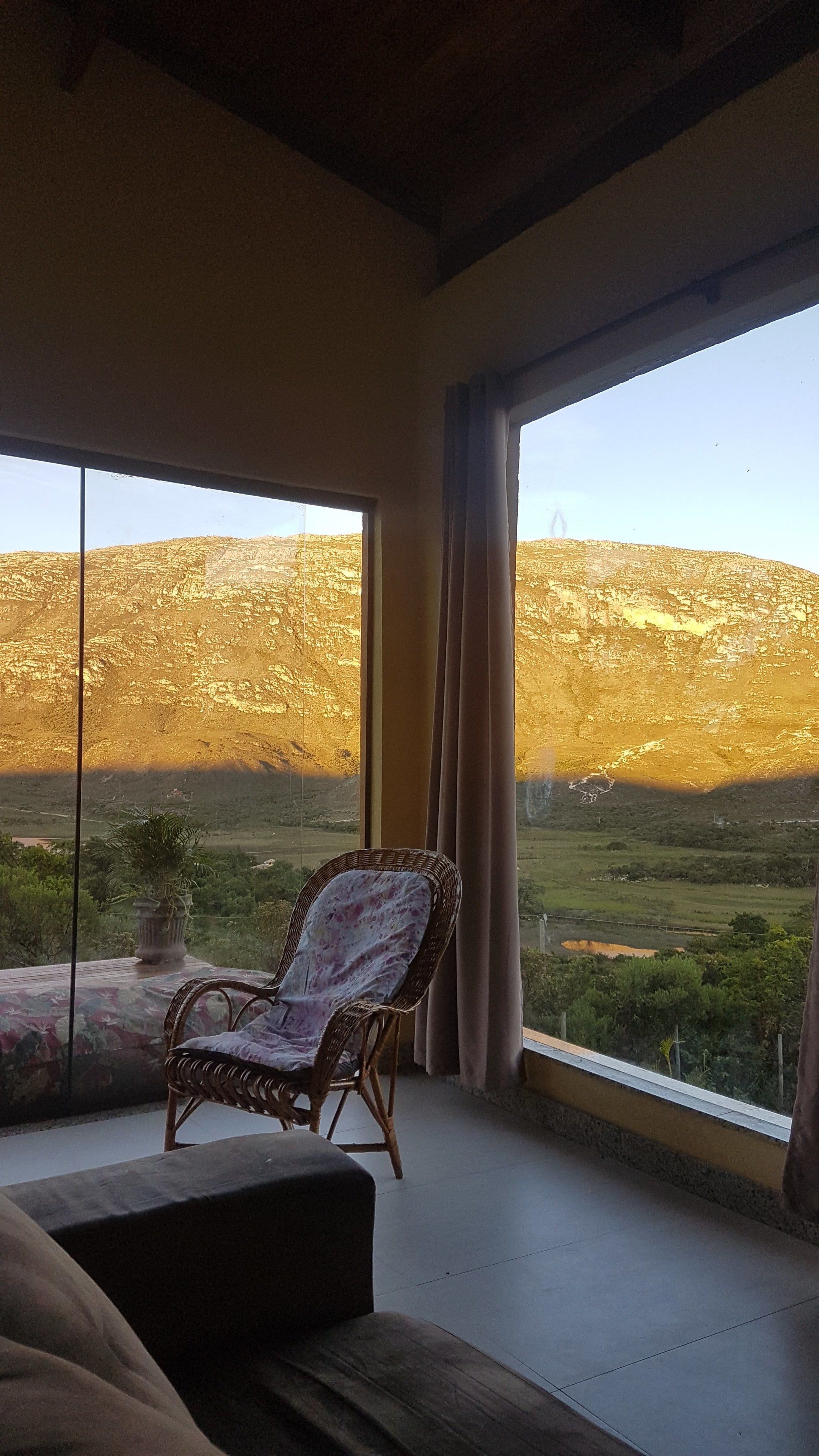 Una stanza con una grande finestra, una sedia in vimini e vista su un paesaggio montuoso.