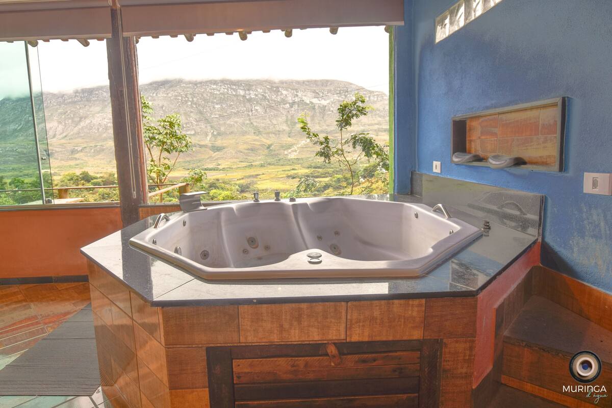 A bathroom with a large bathtub, a view of a mountainous landscape, and a blue wall.