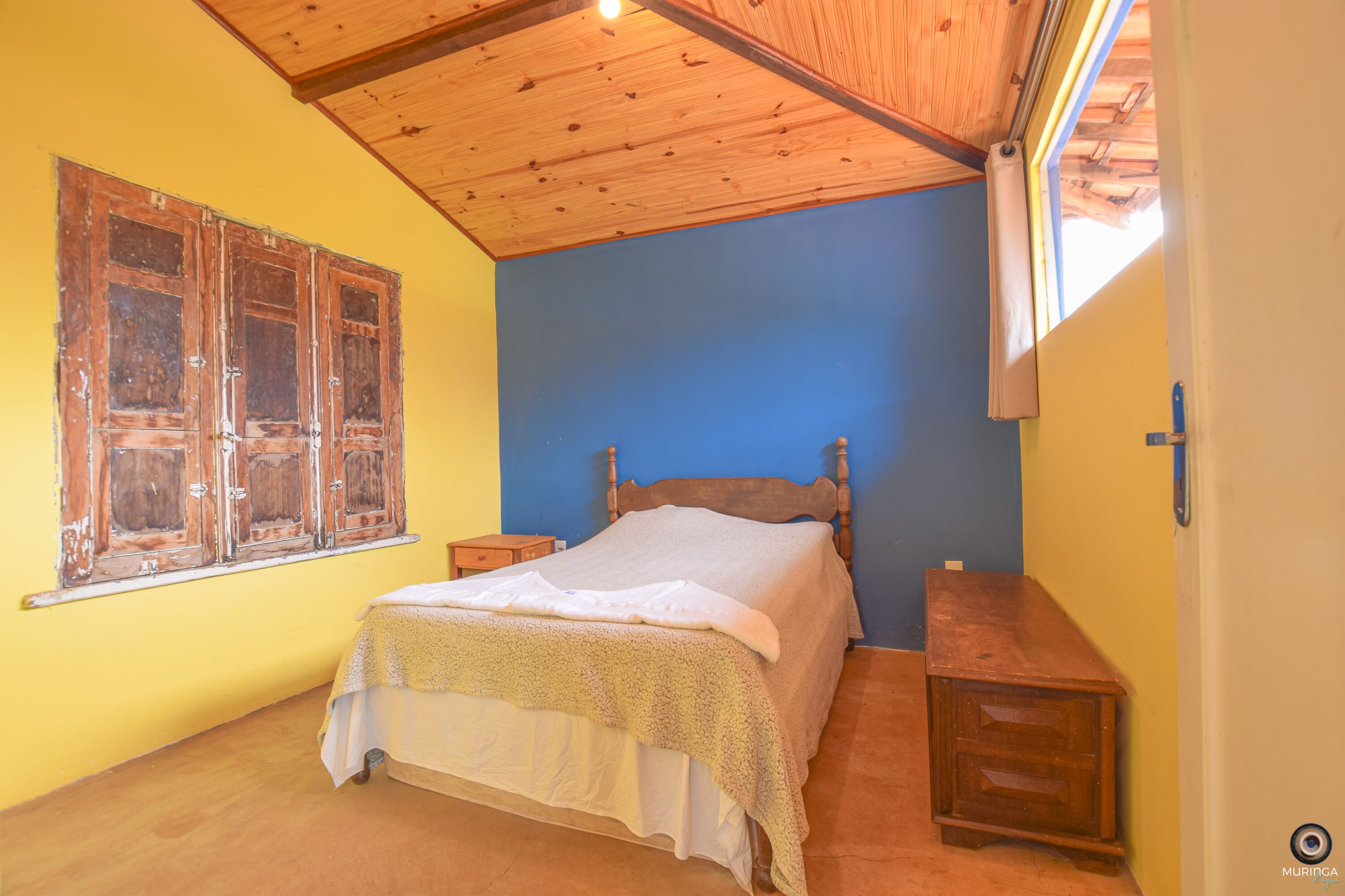 A bedroom with a wooden bed, a nightstand, a wooden dresser, and a window with wooden shutters.