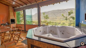 Un baño moderno con un jacuzzi de vidrio, suelo de madera y vistas a un paisaje montañoso.