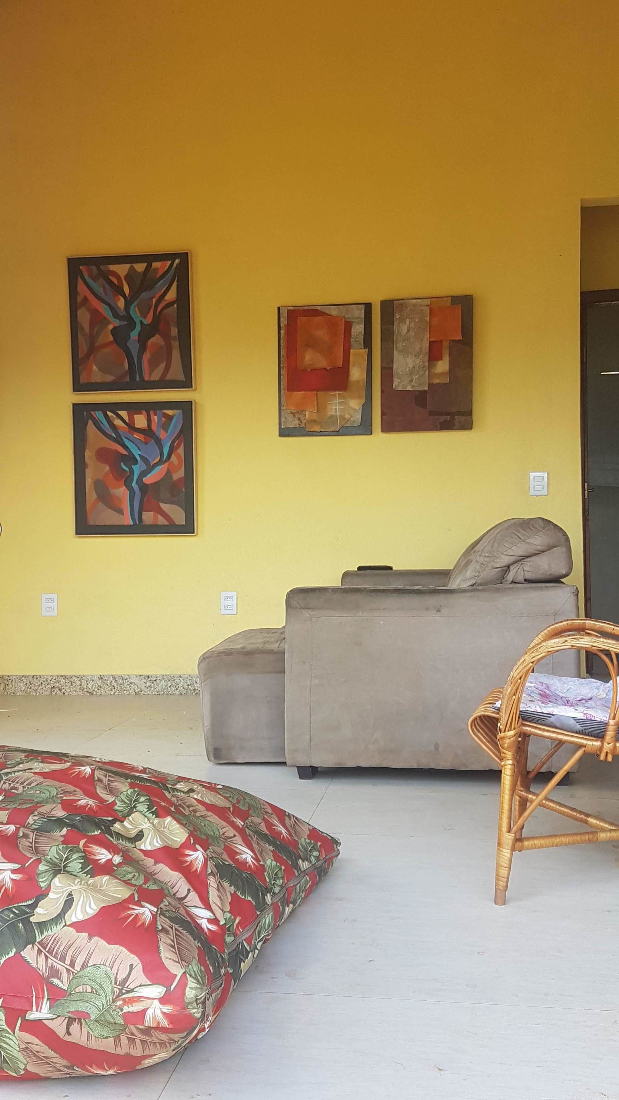 Un salon comprenant un canapé, un fauteuil en osier et trois tableaux abstraits accrochés au mur.