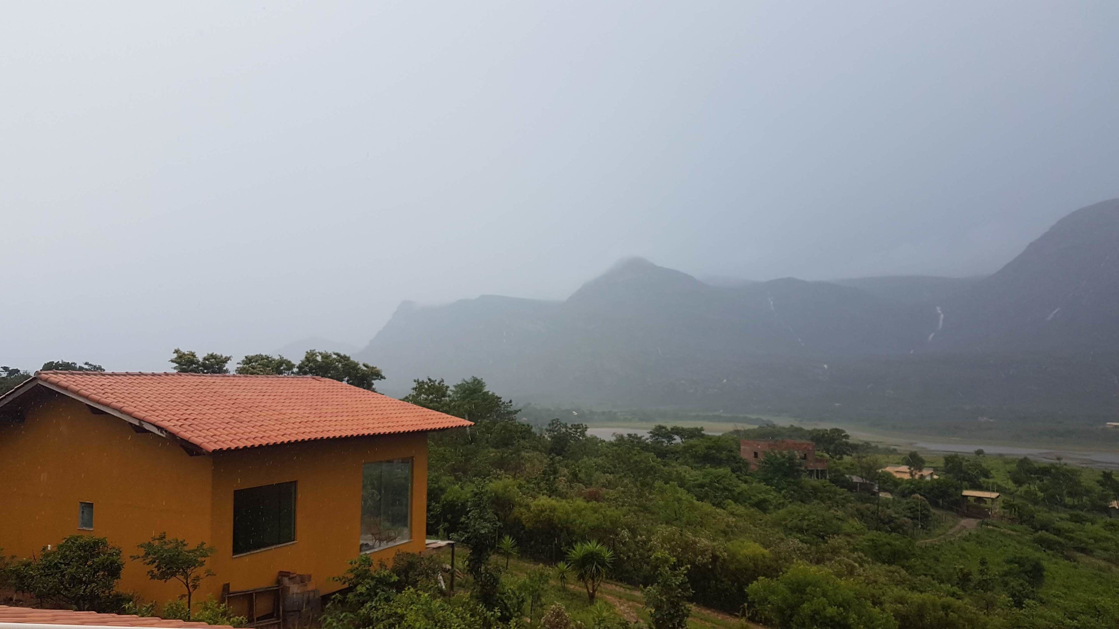 A yellow building with a red roof, surrounded by lush greenery and mountains in the background.