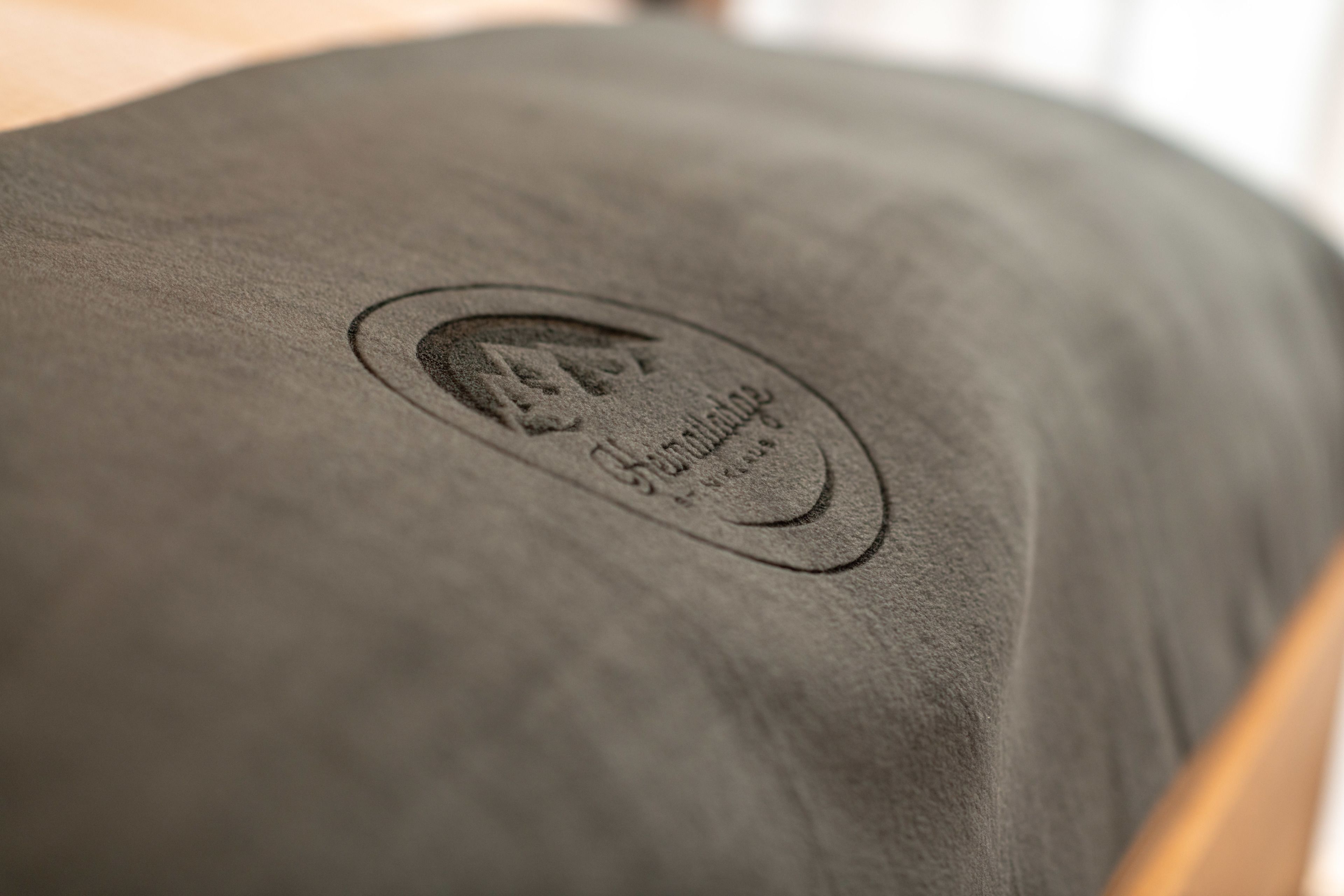 A close-up of a grey upholstered headboard with an embossed logo and text.
