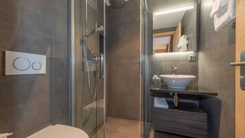 Un baño moderno con cabina de ducha de vidrio, lavamanos blanco y tocador de madera.
