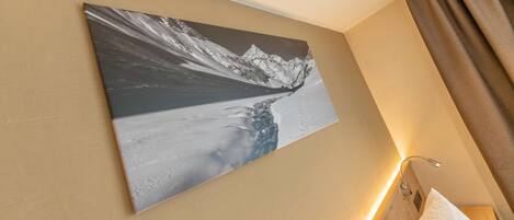 Ein Hotelzimmer mit großem Landschaftsbild von Bergen an der Wand, einem Bett mit weißer Bettwäsche und einem Holz-Kopfteil.