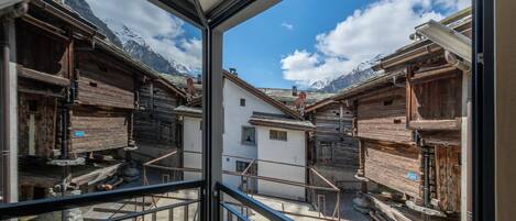 Ein traditionelles Holzchalet vor einer Bergkulisse, sichtbar durch ein Fenster.