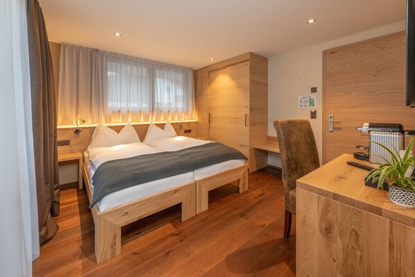 A modern bedroom with a wooden bed, bedside tables, a desk, and a potted plant.