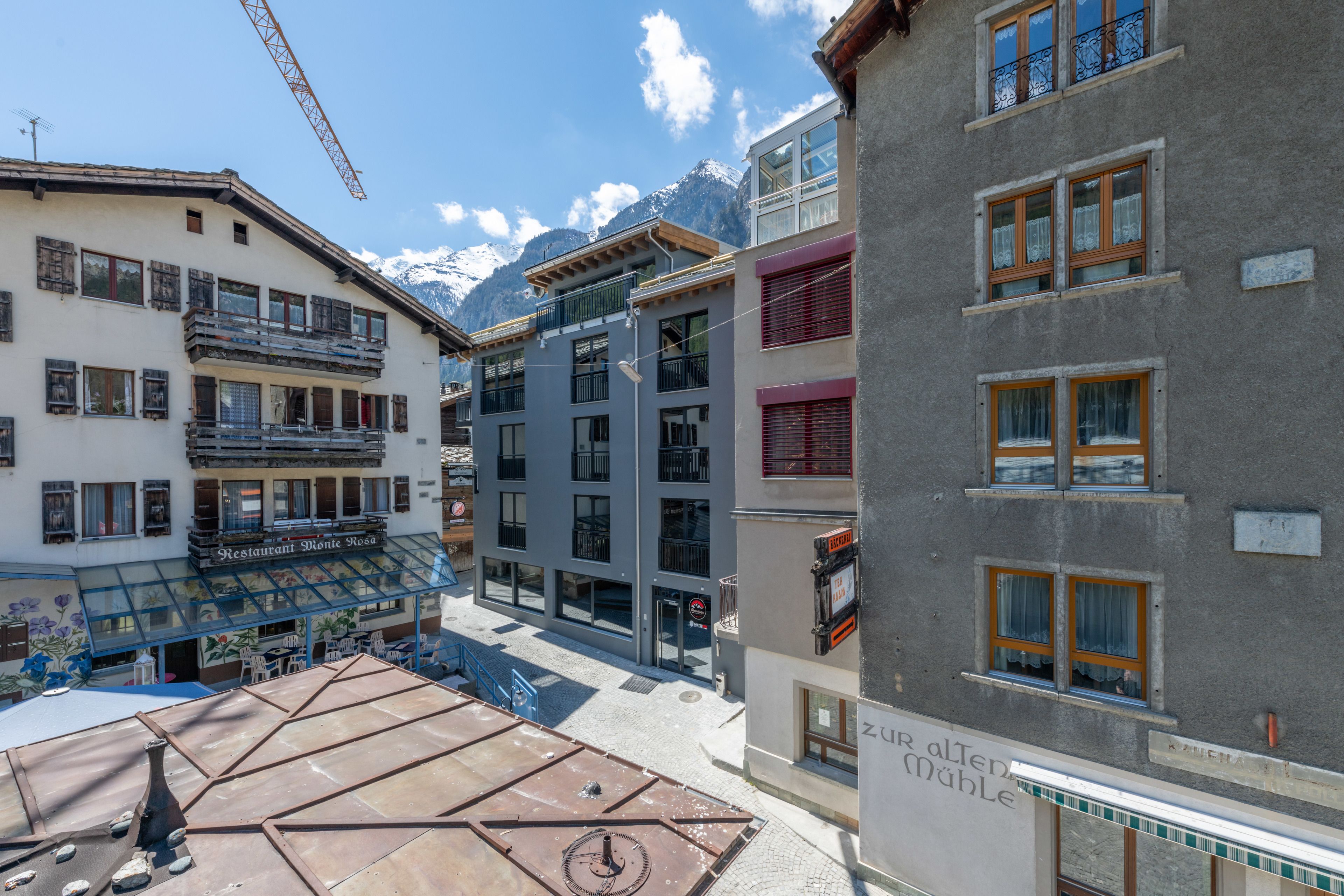 A hotel with a glass facade, balconies, and a view of snow-capped mountains.