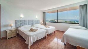 A hotel room with two beds, a nightstand with a lamp, and a view of the sea.