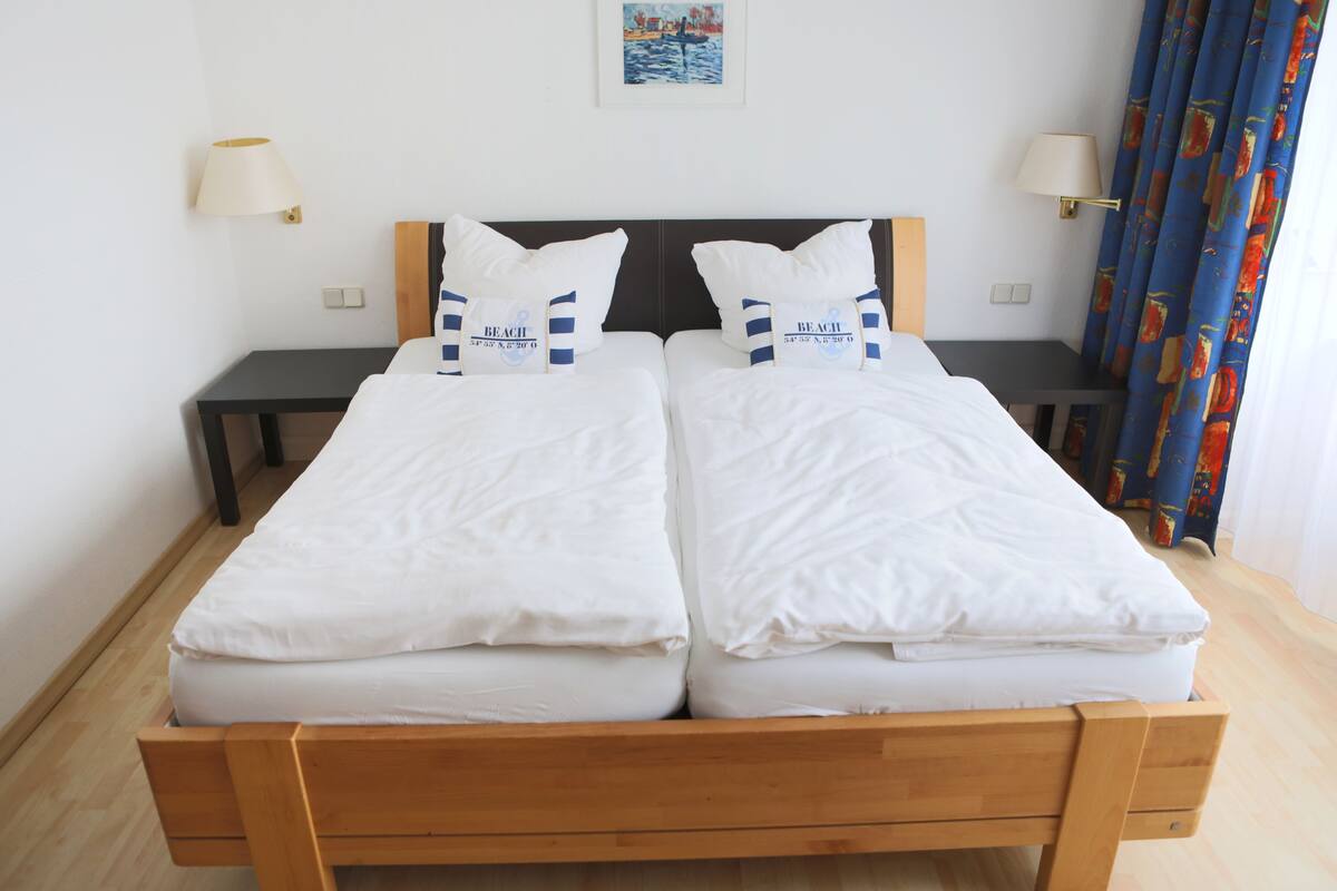 A double bed with white bedding and matching pillows, two bedside tables, and a nightstand.