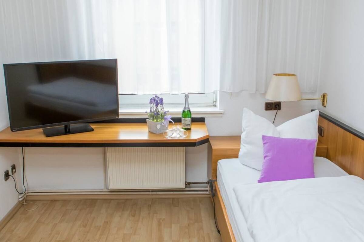 A hotel room with a bed, a TV, a desk, a lamp, and a window with curtains.
