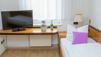 Ein Hotelzimmer mit Bett, Fernseher, Schreibtisch, Lampe und einem Fenster mit Vorhängen.